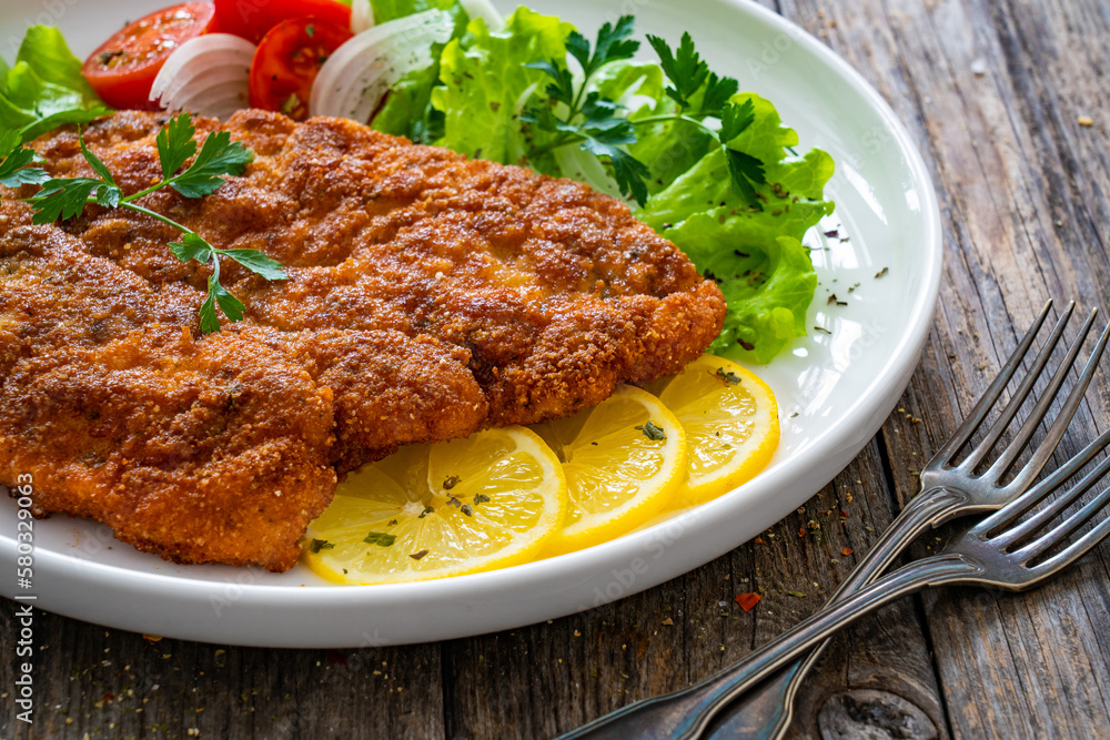 Breaded fried pork chop with cabbage salad and greens on wooden table
