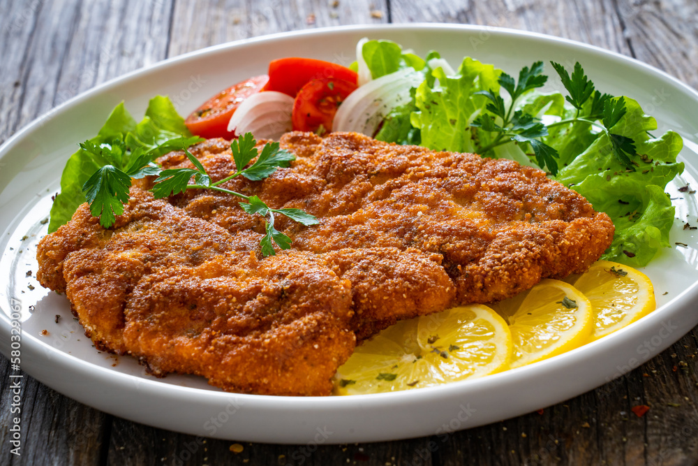 Breaded fried pork chop with cabbage salad and greens on wooden table
Breaded fried pork chop with cabbage salad and greens on wooden table