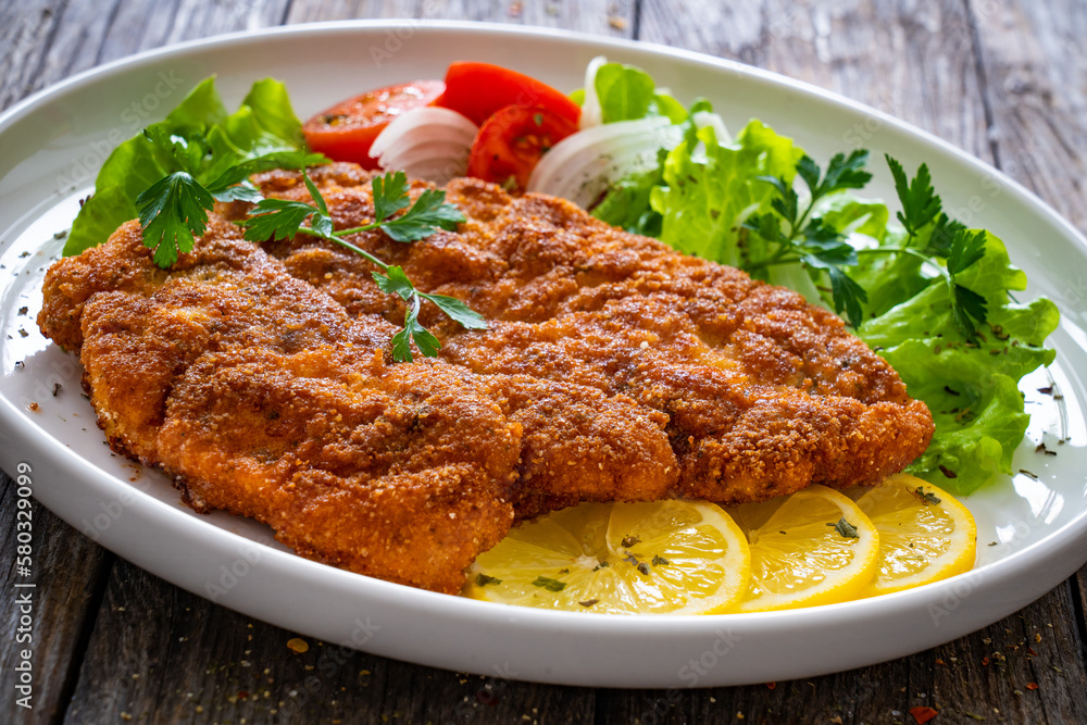Breaded fried pork chop with cabbage salad and greens on wooden table
Breaded fried pork chop with cabbage salad and greens on wooden table