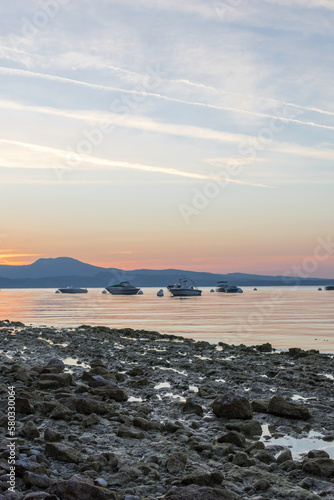 Morning atmosphere at Lake Garda. The water level is historically low, so rocks and stones on the shore stand out. In the background the water, boats, buoys and the shore in the morning light