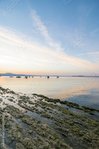 Morning atmosphere at Lake Garda. The water level is historically low, so rocks and stones on the shore stand out. In the background the water, boats, buoys and the shore in the morning light