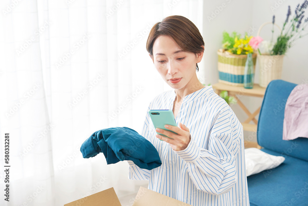 スマートフォンと洋服を持つ女性　ネットショッピング・フリマアプリ・洋服レンタル