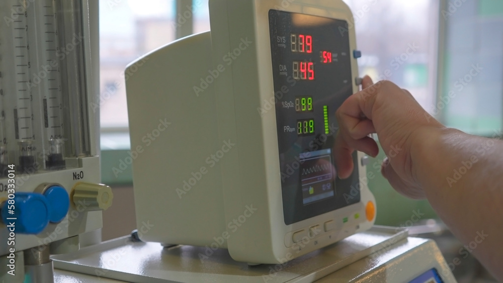 Use of a medical electrocardiograph in the operating room. The hand of a medical worker in a glove. Modern medical equipment and instruments. Measurement of pressure to the patient during surgery. Use of a medical electrocardiograph in the operating room. The hand of a medical worker in a glove. Modern medical equipment and instruments. Measurement of pressure to the patient during surgery.