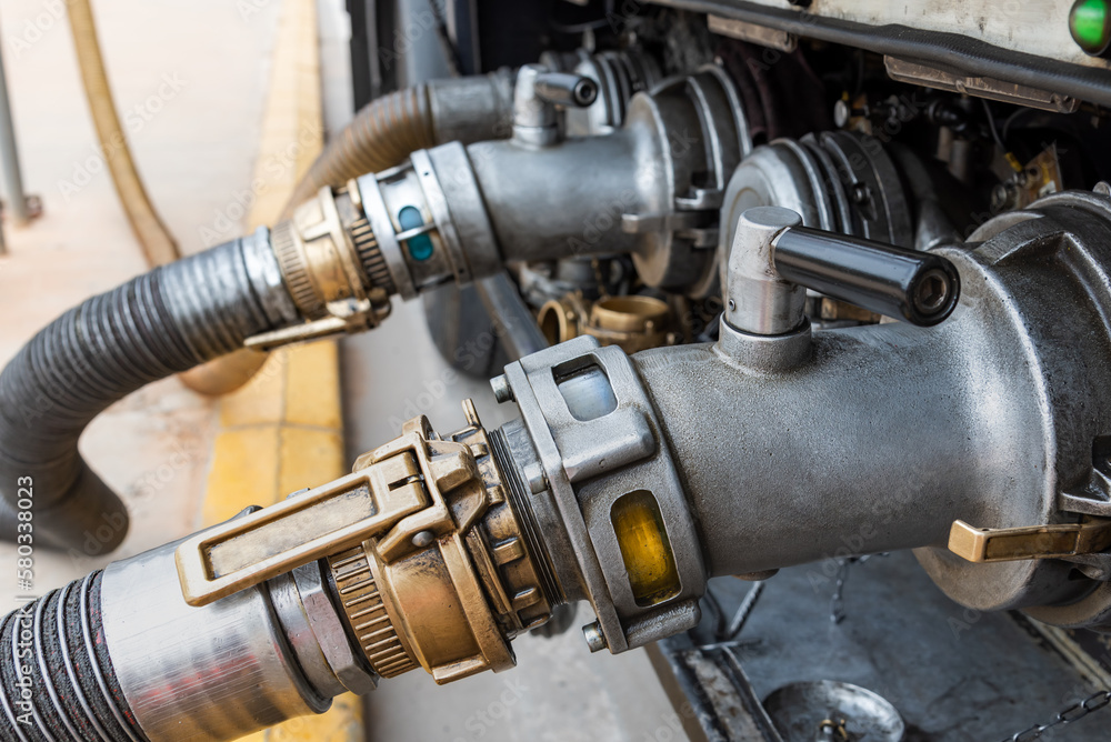 Devices attached to the mouths of a tanker truck to connect the discharge hoses,discharging diesel and gasoline in the background.