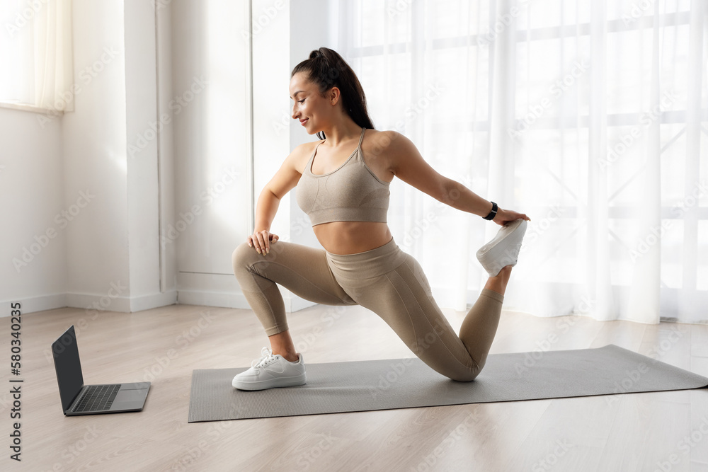Side view of athletic woman training at home, using laptop Side view of athletic woman training at home, using laptop
