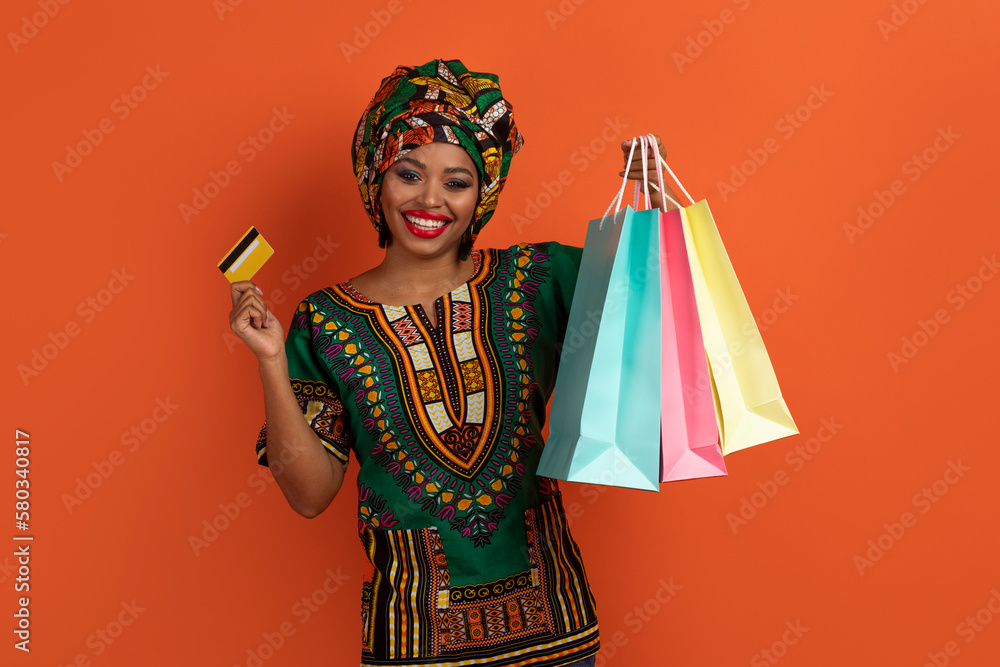 Cheerfy black lady showing colorful shopping bags and bank card