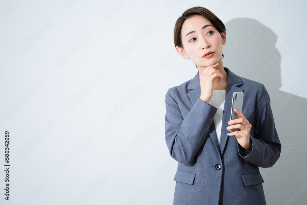 スマートフォンを持ちながら考え込んでいる若い女性　ビジネスイメージ