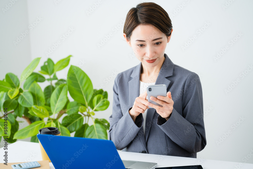 ノートパソコンとスマートフォンを使う若い女性　ビジネスイメージ