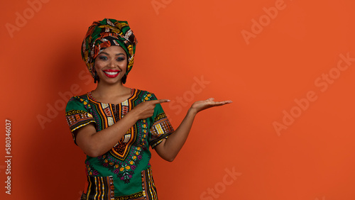 Happy attractive african woman in national costume showing something nice