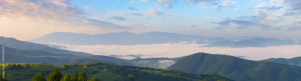 Obraz premium colorful foggy sunrise in mountainous rural area. panorama with forested hills covered in morning mist. dramatic clouds above the distant ridge. travel background