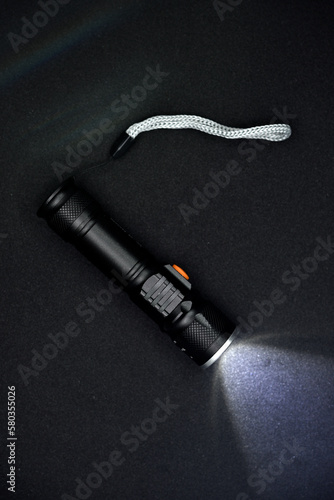 Metal black flashlight on a black background. Burning pocket flashlight close-up. Lighting device.