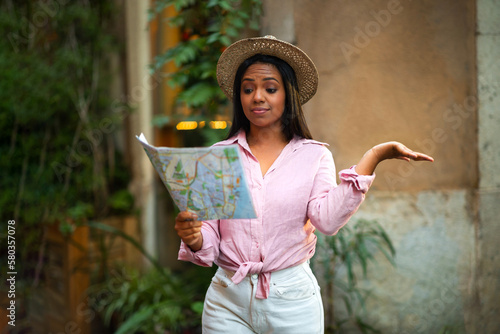 Confused sad young african american woman in hat looking at map in city, hold on hand free space, outdoor #580357078