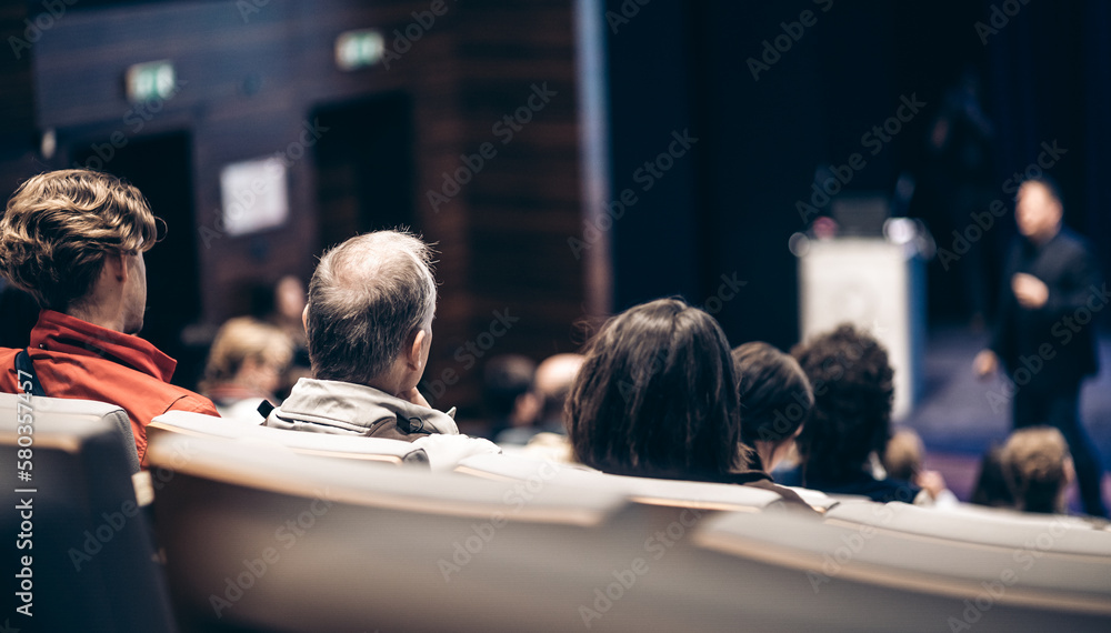 Speaker giving a talk in conference hall at business event. Rear view of unrecognizable people in audience at the conference hall. Business and entrepreneurship concept Speaker giving a talk in conference hall at business event. Rear view of unrecognizable people in audience at the conference hall. Business and entrepreneurship concept