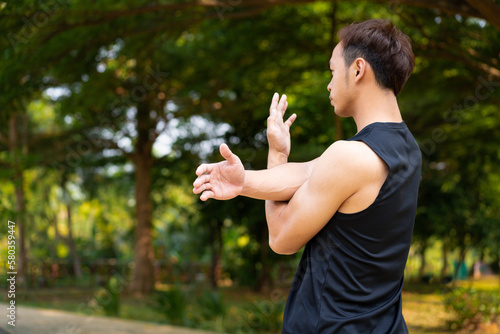 sporty handsome Asian man stretching arms before jogging in city public park during summer day, young guy spend quality time on weekend workout outdoor in nature for healthy and active lifestyle