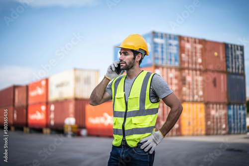 Canvas-taulu Caucasian warehouse worker in uniform with hard hat using mobile phone standing in container port terminal