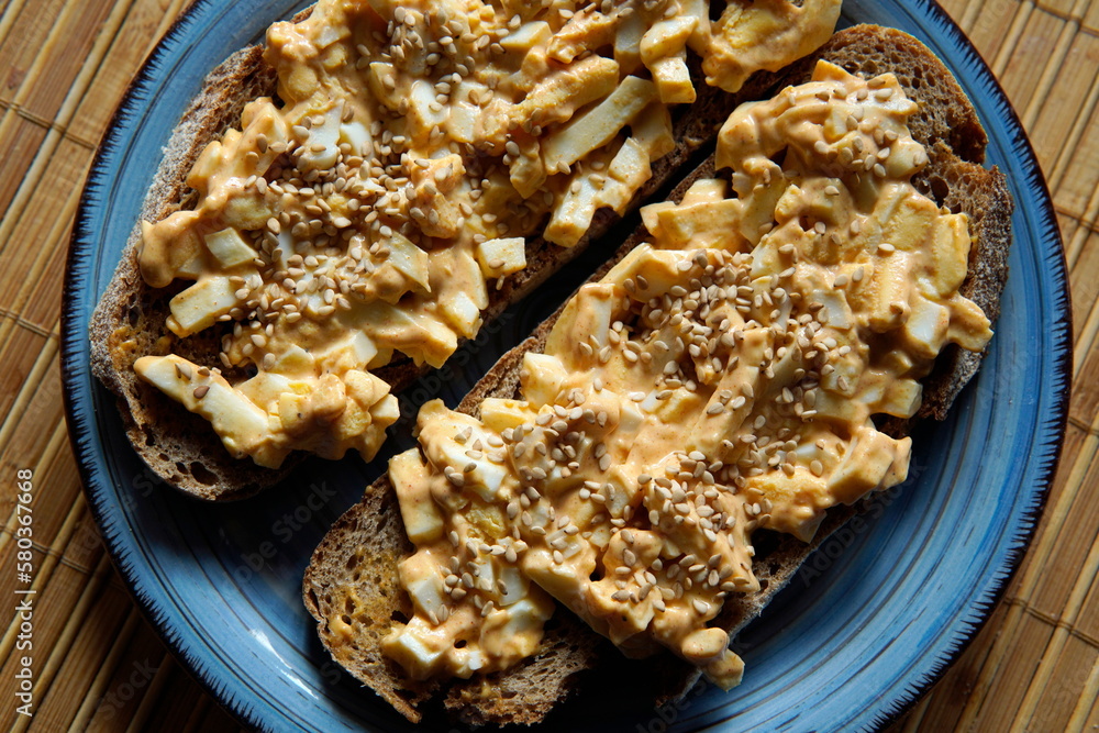Scheibe Bauernbrot mit Eiersalat und Sesam auf blauem Keramikteller