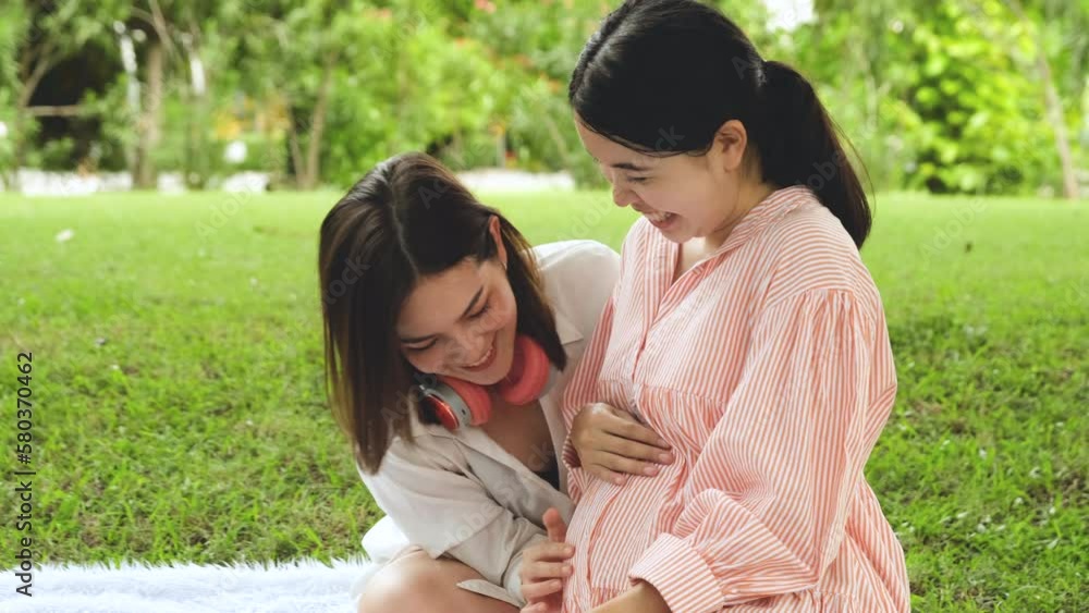 Asian lesbian couples or sisters who got pregnant by artificial insemination are sitting warmly chatting and smiling in a park. Asian lesbian couples or sisters who got pregnant by artificial insemination are sitting warmly chatting and smiling in a park.