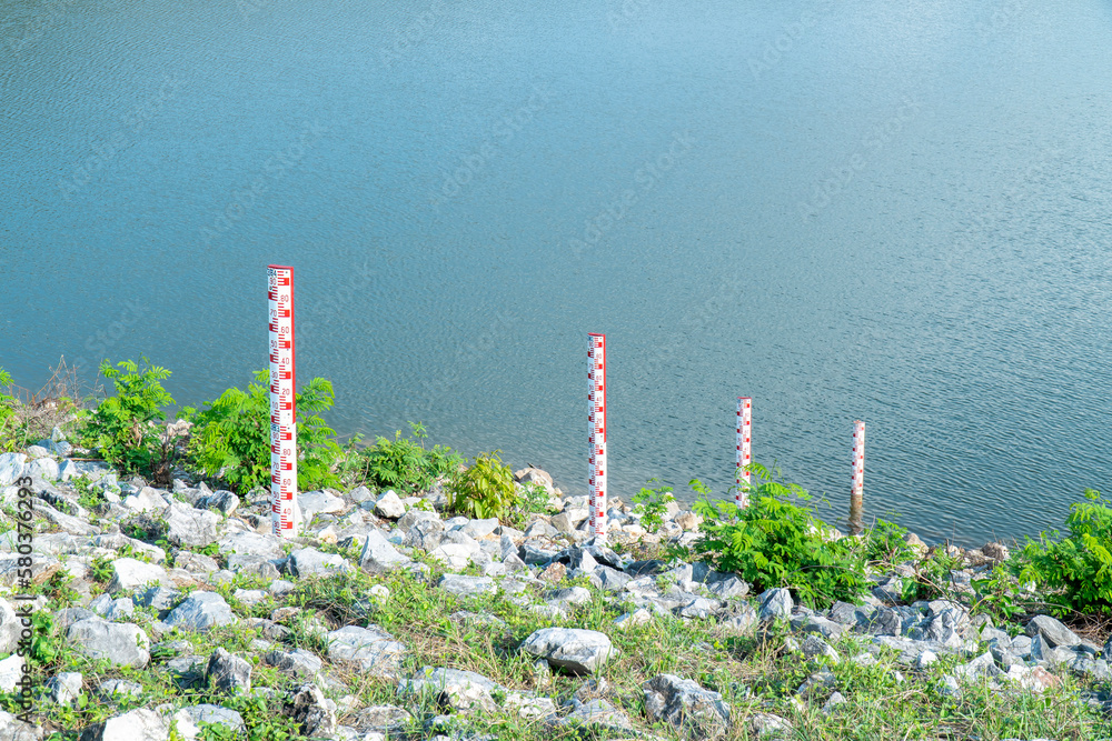 Staff gauge water at dam background. Four red water level gauge scale at lake - obrazy, fototapety, plakaty 