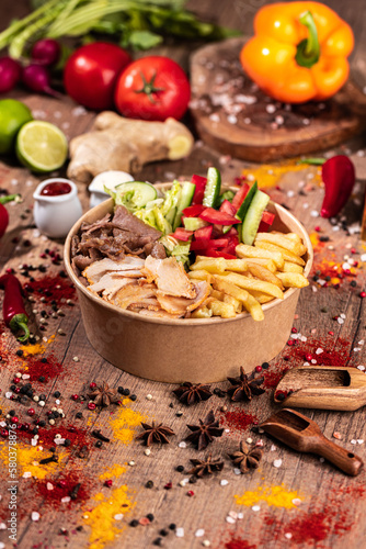 Doner Kebab Bowl with Mixed Meat, Fries, and Fresh Vegetables.
Colorful doner bowl featuring a mix of sliced chicken and beef, served with French fries, lettuce, tomatoes, cucumbers, and red peppers. 