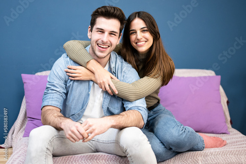 Portrait of a happy young couple seated on couch and smiling. Cheerful friends having fun at home. Love and friendship concept