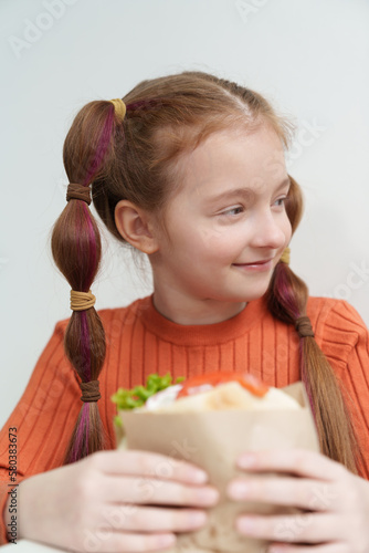 Cute elementary age girl with ponytails eating a sandwich in fast food restaurant. Adorable Ukrainian child eats pita souvlaki dish in Greek cafe