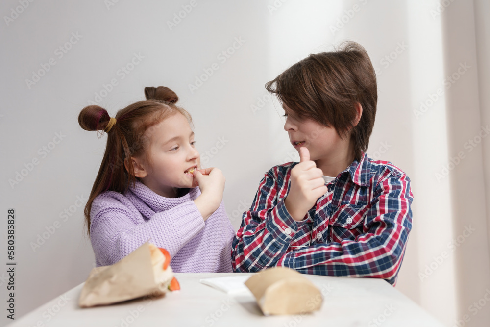 Cute white kids looking at each other while eating fries in a fast food restaurant. Couple of adorable elementary age children enjoying the lunch in a cafe Cute white kids looking at each other while eating fries in a fast food restaurant. Couple of adorable elementary age children enjoying the lunch in a cafe
