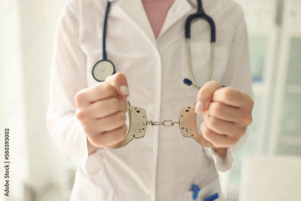 Doctor with stethoscope in handcuffs close-up. Nurse with metal handcuffs on her hands.