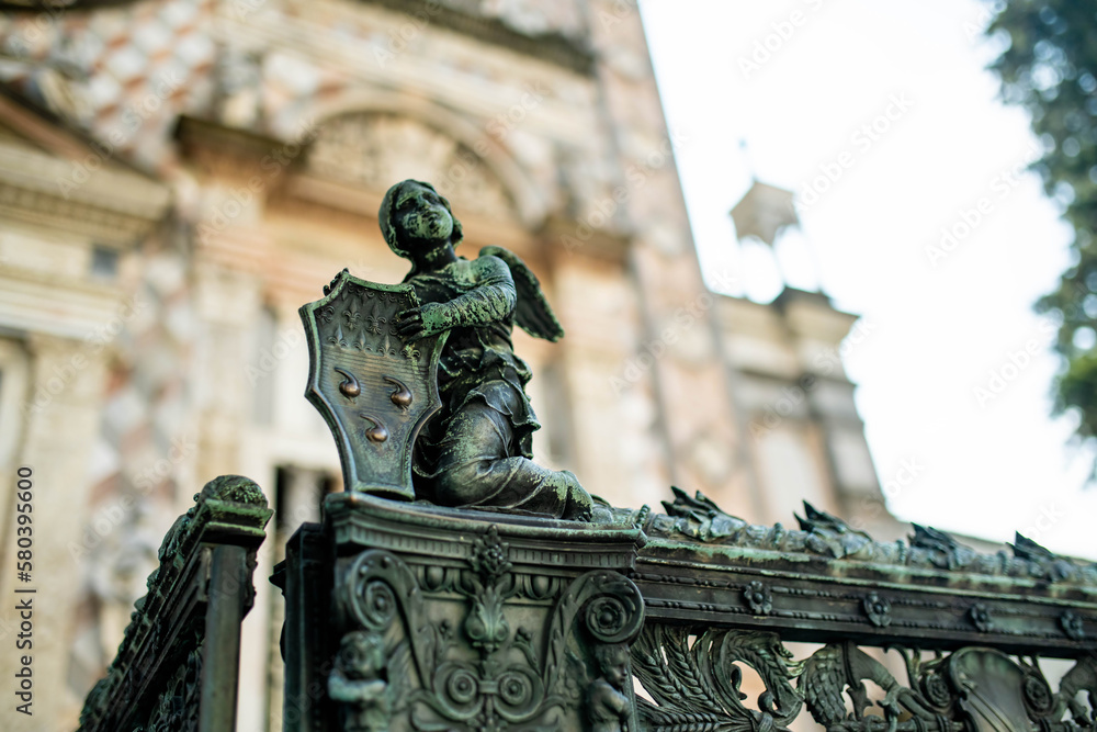 Naklejka premium Metal shield held by an angel statue as a gate decoration on medieval streets of Bergamo city northeast of Milan. Scenic views of Citta Alta, town's upper district. Bergamo, Italy.