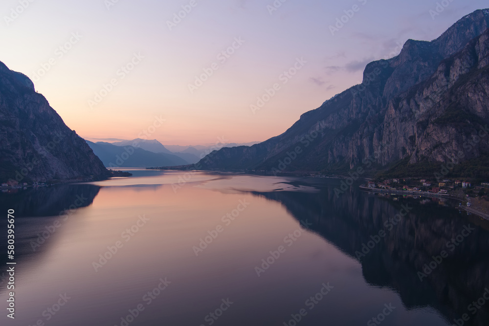 Beautiful aerial view of the famous Como Lake on purple sunset. Mountains reflecting in calm waters of the lake with Alp mountain range on the background.