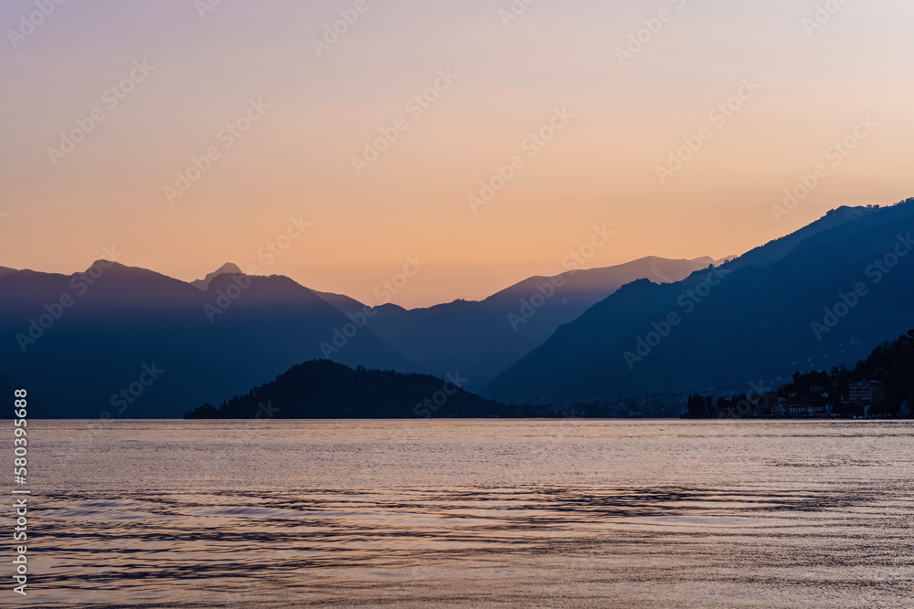 Beautiful aerial view of the famous Como Lake on purple sunset. Clouds reflecting in calm waters of the lake with Alp mountain range on the background.