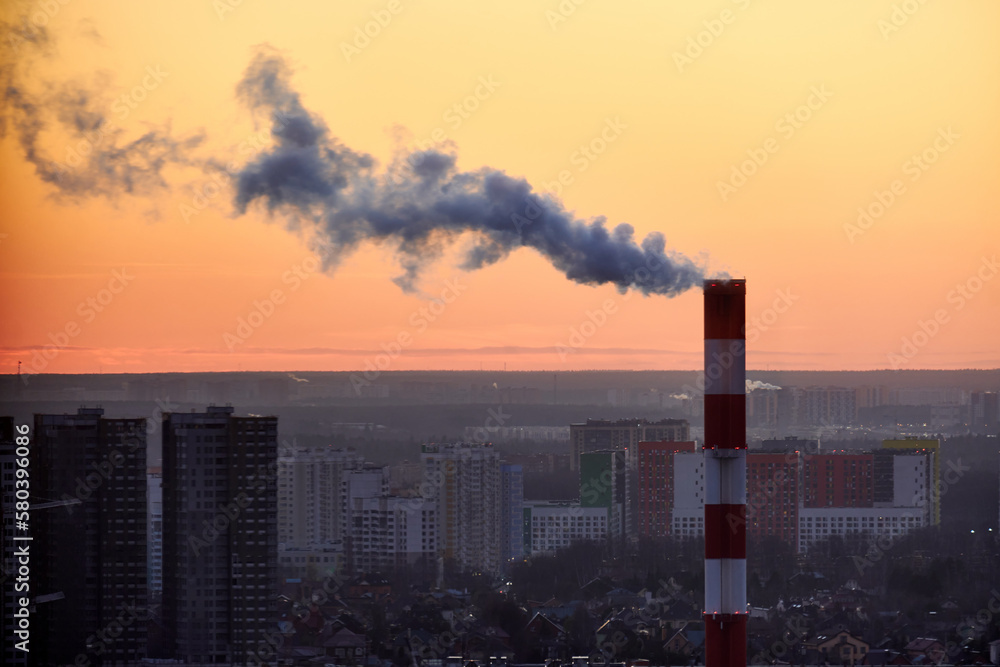 Smoke from a tall chimney over a winter city with houses in the snow