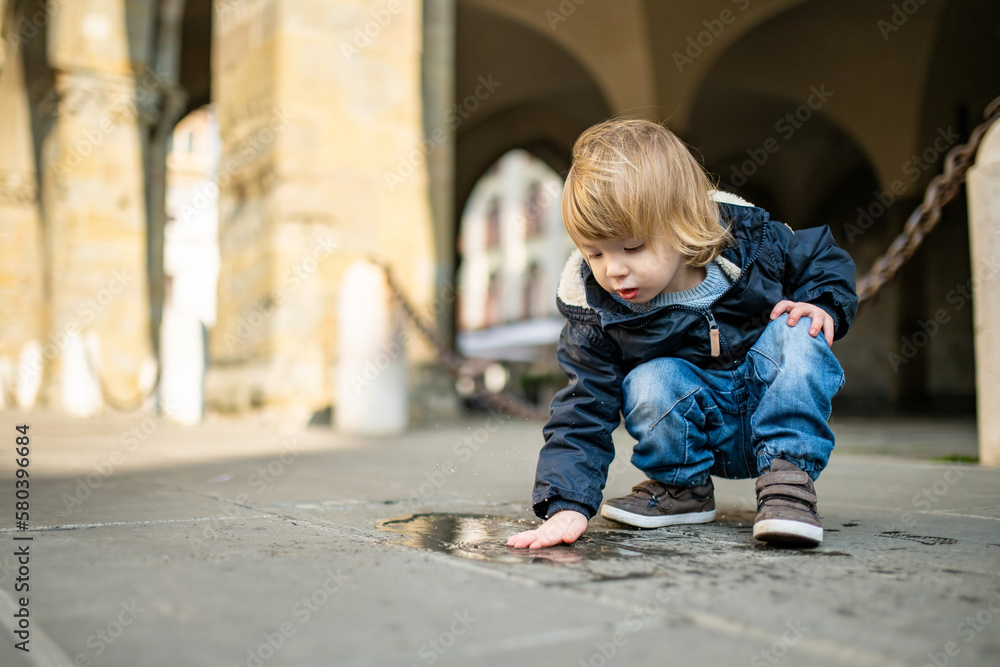 Cute toddler boy playing in a puddle on the street of Bergamo. Little child having fun exploring in Citta Alta, upper district of Bergamo. Bergamo, Italy. Cute toddler boy playing in a puddle on the street of Bergamo. Little child having fun exploring in Citta Alta, upper district of Bergamo. Bergamo, Italy.