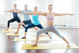 Four people in yoga class in Warrior II pose stretching their arms