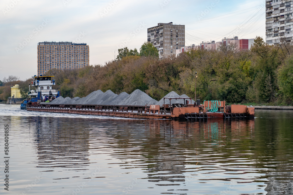 Obraz premium Barge loaded with sand or grey gravel floats on wide river