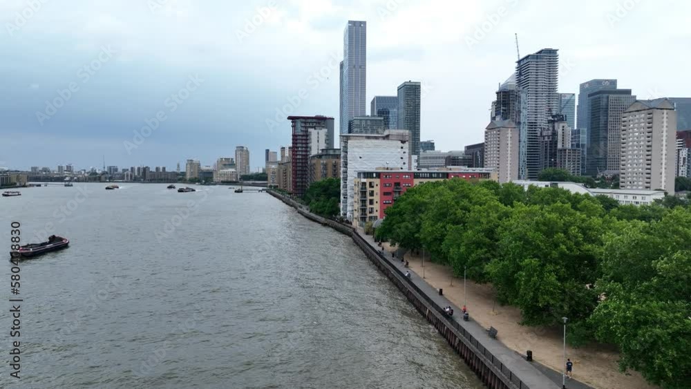Trees in park on riverbank and high rise buildings on cloudy day. Aerial sliding reveal of Thames river with boats on water surface. London, UK Trees in park on riverbank and high rise buildings on cloudy day. Aerial sliding reveal of Thames river with boats on water surface. London, UK