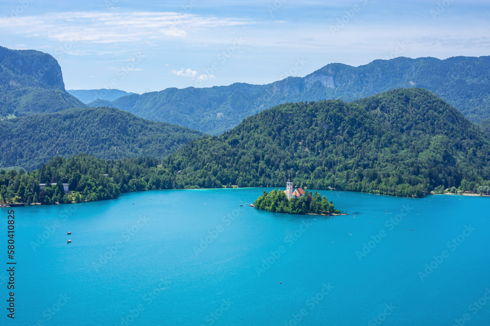A small island with a church and green trees in a lake surrounded by high mountains, Bled, Slovenia
