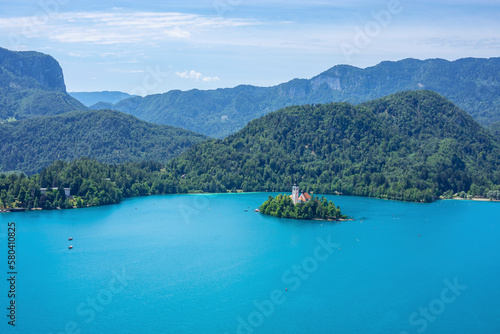 A small island with a church and green trees in a lake surrounded by high mountains, Bled, Slovenia 