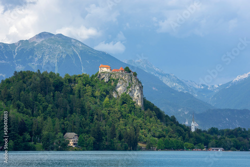 Lake Bled at sunny day with high mountains, green trees and castle on the cliff top, Slovenia
