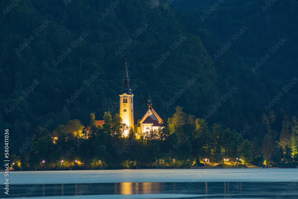 A small island by night with a church and green trees in a lake surrounded by high mountains, Bled, Slovenia
