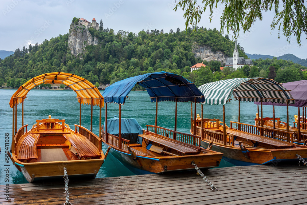Small wooden gondola boats rest moored at Lake Bled with castle in the background, Slovenia
