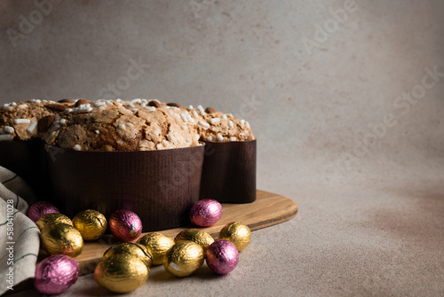 Easter dove cake with chocolate Easter eggs wrapped in foil on wooden cutting board, striped napkin on concrete background, copy space