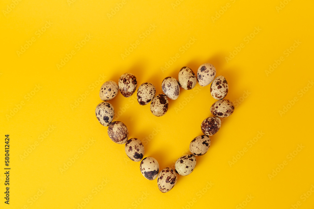 Easter holiday card. Symbol of love. Heart shape made of marble quail eggs on yellow background. Mockup design. Postcard. Healthy organic food. Empty text place. Proper nutrition. Copy space Easter holiday card. Symbol of love. Heart shape made of marble quail eggs on yellow background. Mockup design. Postcard. Healthy organic food. Empty text place. Proper nutrition. Copy space