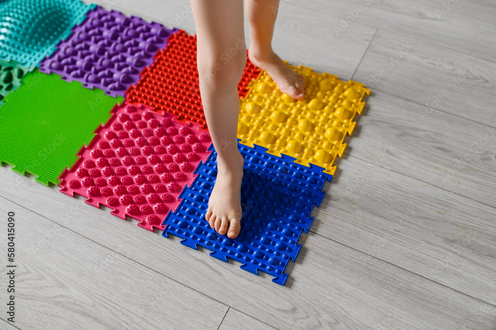 The child walks on an orthopedic massage mat for feet. Massage mats