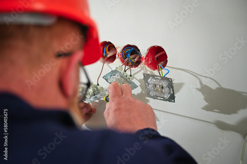 Professional electrician technician installing a wall socket in a new house. Electrical repairs at home. Electrician mounting wiring for electric sockets. photo