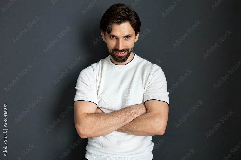 Portrait of cunning sly athletic brutal manly bearded guy in white t-shirt standing with crossed hands against black studio background, looking at camera with smile, challenging you Portrait of cunning sly athletic brutal manly bearded guy in white t-shirt standing with crossed hands against black studio background, looking at camera with smile, challenging you