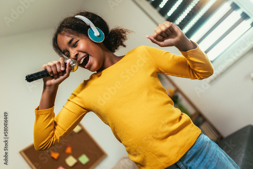 Tableau sur toile Cute preteen black girl  holding microphon singing karaoke at home, recording songs for contest