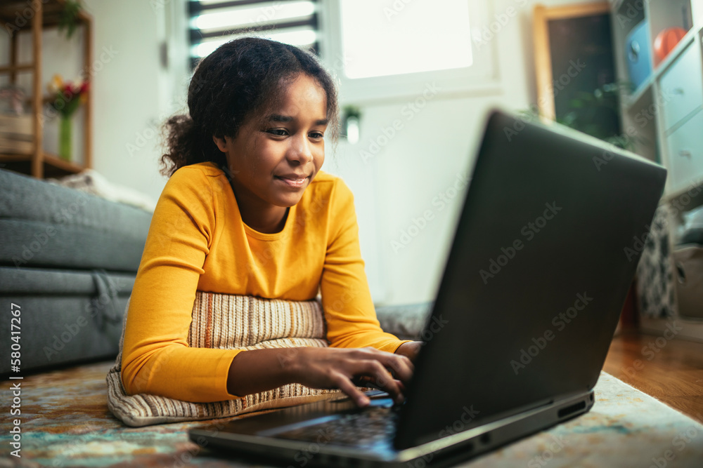 Smiling school African American girl watching the video lesson on computer,happy child have online web class using laptop at home, homeschooling concept Smiling school African American girl watching the video lesson on computer,happy child have online web class using laptop at home, homeschooling concept