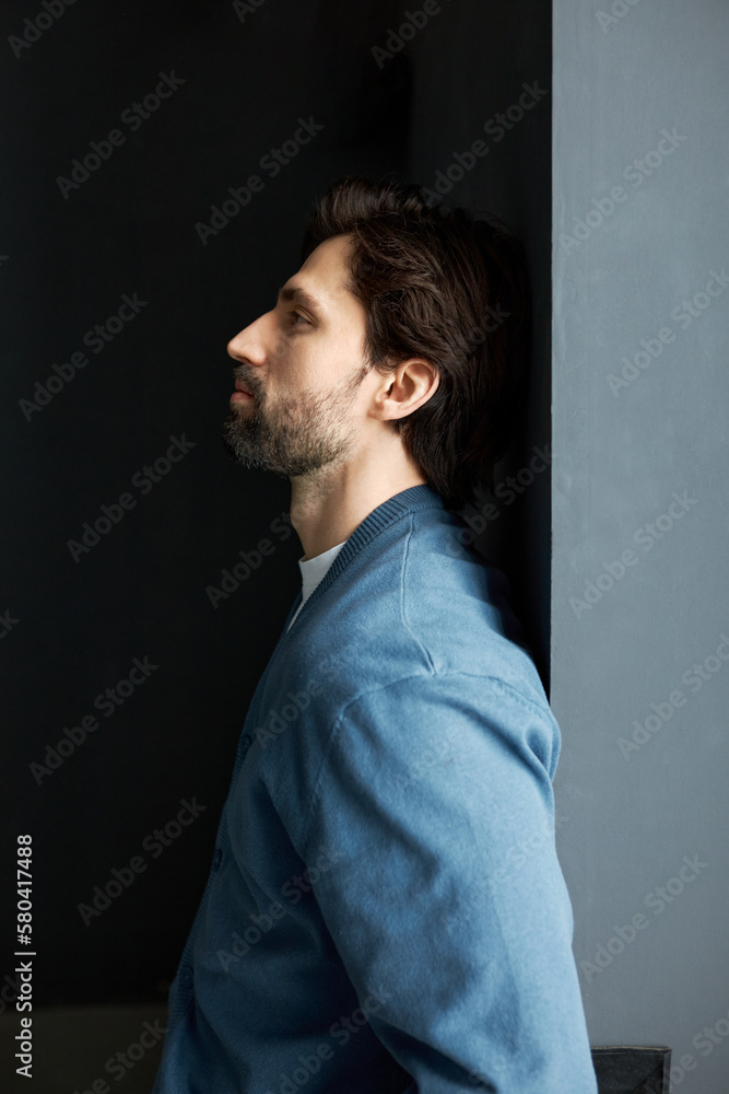 Profile view of disappointed frustrated offended businessman or invest trader in blue cardigan leaning against gray wall looking aside with frustration, unsatisfied with results of business meeting