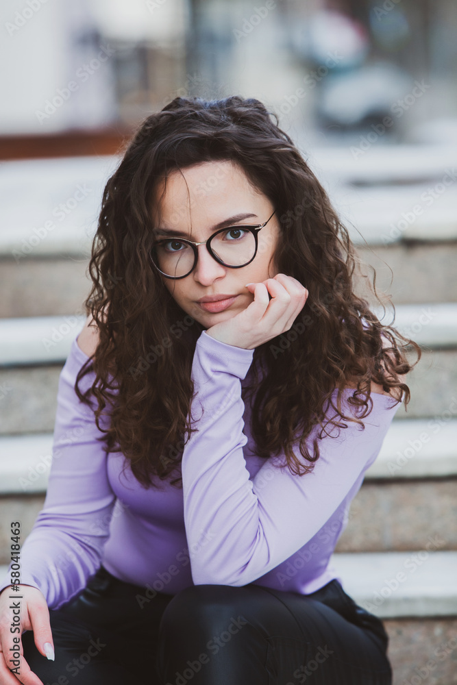 Beautiful young woman with brunette curly hair, portrait in eye glasses enjoying the sun in the city. Beautiful young woman with brunette curly hair, portrait in eye glasses enjoying the sun in the city.