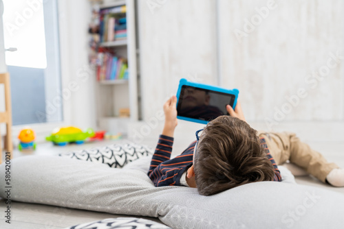 One child a boy laying on the floor and playing games on tablet, using technology and early child development concept